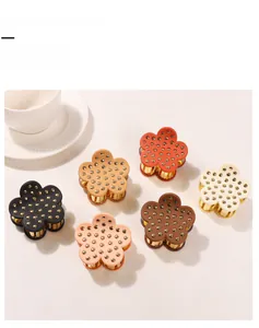 Detail of six colorful floral hair claw clips with golden studs on a beige background