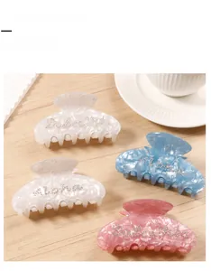 Detail of colorful marble acetate hair claws with rhinestone lettering on wood surface