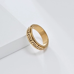 Détail d'une bague dorée avec motif clé grecque et texture en métal brossé