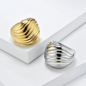 Chunky stainless steel wave textured rings in gold and silver finish on a white pedestal