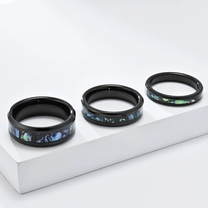 Polished black tungsten rings with colorful abalone shell inlay on white pedestals