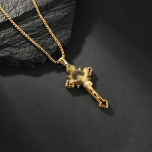 Detail of a gold-plated box chain with a vintage-style cross pendant on a dark rock surface