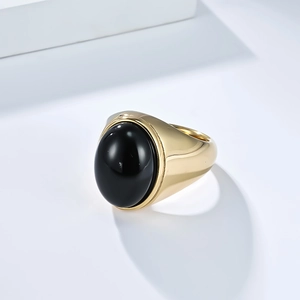 Macro d'une bague large dorée avec une pierre noire ovale polie sur fond blanc minimaliste