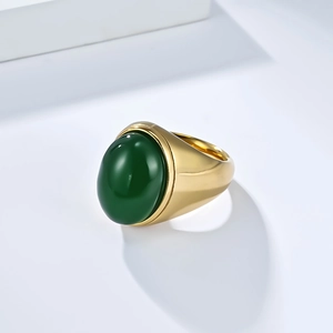 Vue détaillée d'une bague dorée en acier avec pierre verte sur décor blanc