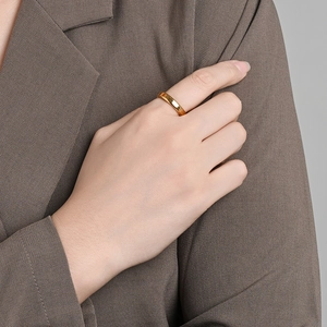 Close-up of a minimalist gold domed titanium ring worn on a finger over a brown suit