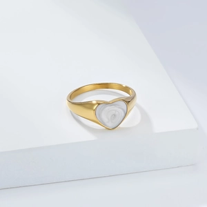Elegante anillo de acero de titanio dorado con corazón de esmalte blanco en soporte minimalista