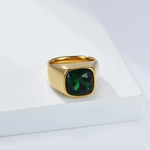 Gros plan d'une bague chevalière dorée avec une pierre précieuse verte sur support blanc