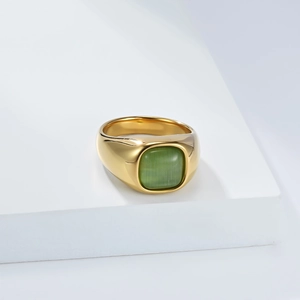 Detail of a gold wide band ring featuring a square green cat-eye stone on a white stand