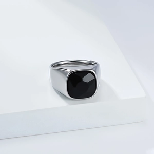 Gros plan d'une bague chevalière argentée avec une pierre noire carrée sur un piédestal