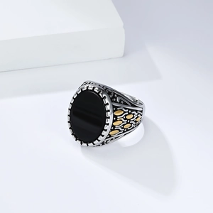 Détail d'une bague vintage pour homme avec pierre noire ovale et accents de feuilles d'or