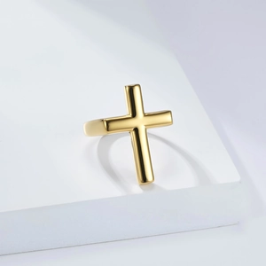 Bague croix pour homme en acier inoxydable doré poli sur un support d'exposition blanc