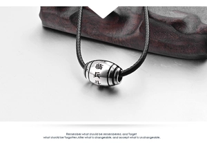 Macro shot of stainless steel barrel bead with engraved Nine Syllable Mantra and black cord