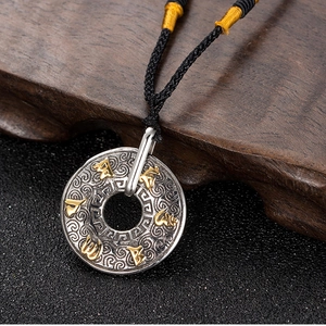 Détail macro du pendentif vintage en acier titane avec mantra à six mots et nuages gravés