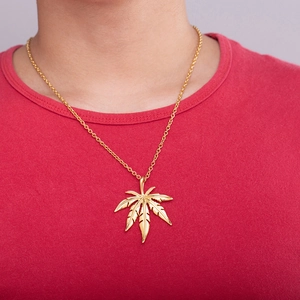 Gros plan d'un pendentif feuille d'érable dorée sur une fine chaîne et un t-shirt rouge