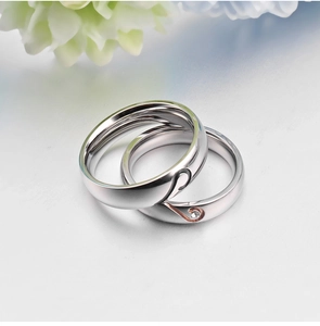 Polished stainless steel couple rings with heart design and diamond inlay on light surface