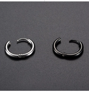 Detail of silver and matte black stainless steel hinged hoop earrings on textured surface