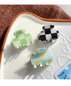 Three acetate checkerboard hair clips in green, black, and blue on a ceramic plate
