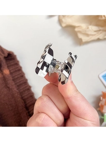 Close-up of a mini checkered acetate hair claw clip with black and white patterns