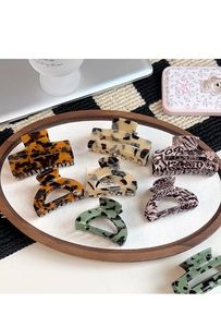Flat lay of diverse French leopard acetate hair claws on a round wooden tray on desk
