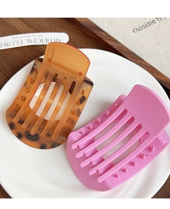 Détail de grandes pinces à cheveux en ambre écaille et rose mat sur une assiette blanche