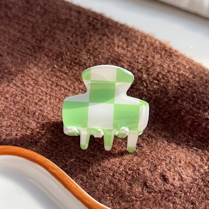 Checkered green and white acetate hair claw clip on brown knit fabric texture
