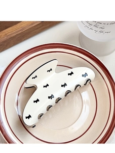 Detailed view of cream-colored resin shark hair claw clip with black puppy pattern