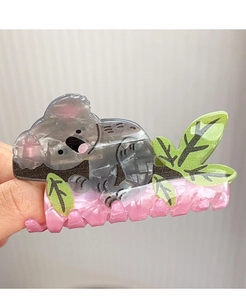 Dettaglio di una pinza per capelli a forma di koala grigio marmo con un ramo verde