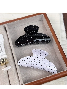 Detail view of retro black and white polka dot hair claws in a brown leather display box