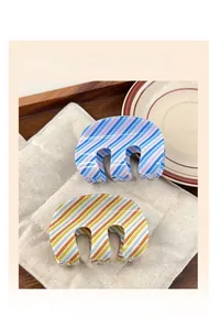 Detail view of striped M-shaped hair claws in pastel colors on a quilted surface
