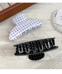 Polished black and white polka dot hair claw clip on white knitted background
