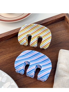 Close-up of stylish M-shaped hair claws with colorful stripes on a wooden tray