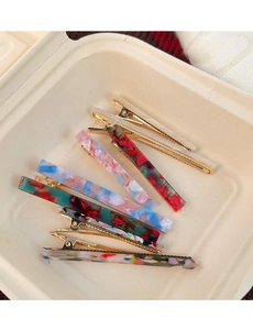 Close-up of marble acetate hair clips in various colors on a soft cream tray display