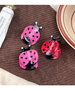Close-up of ladybug hair clips in pink and red acetate with a subtle marble texture