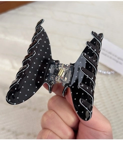 Handheld view of a vintage black butterfly hair claw with white polka dots and clear spring