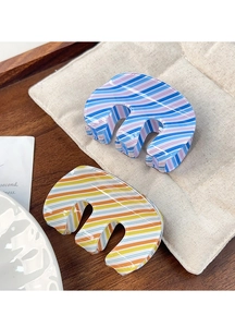 Detail of E-shaped striped hair claws in blue and orange patterns on a rustic surface