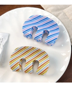 Detail view of colorful striped M-shaped hair claws on a white aesthetic ceramic plate