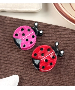 Close-up of pink and red ladybug hair clips made of glossy acetate on brown fabric