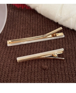 Close-up of gold metal hair clips with white marble texture on a soft knit background