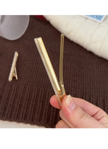 Detail of golden duckbill hair clip with white acetate inlay held by hand