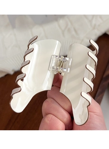 Close-up of a cream-colored acrylic hair claw clip held by hand for size perspective