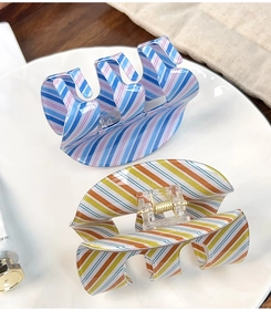 Detail of colorful striped acrylic claw clips with golden metal spring on white plate