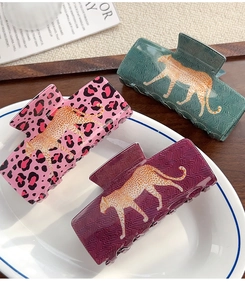 Three elegant leopard print hair claw clips in pink, green, and red with gold leopard accents