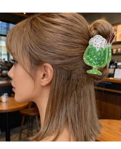 Dettaglio di una molletta per capelli a forma di frappè verde indossata in un caffè