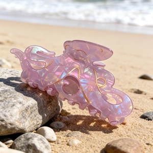 Pince à cheveux pieuvre rose irisée avec motifs dorés sur un rocher de plage