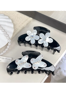 Macro detail of black hair claws featuring white flower and butterfly motifs with rhinestones