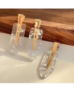 Detail of three resin hair clips with silver foil flakes and golden metal clips on wood