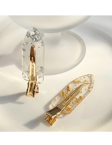 Detail of transparent resin hair clips with gold and silver foil on a ceramic tray