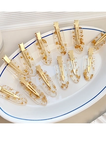 Detailed macro view of transparent acrylic hair clips with gold foil flakes in ceramic tray