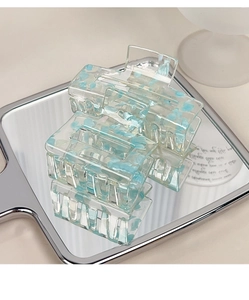 Detail of square acrylic hair claw with blue marble texture on a reflective surface