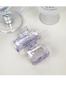 Detail of two transparent acrylic hair claws with purple stone inlay on white surface
